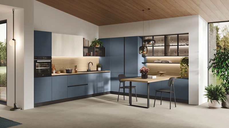 Cucina ad angolo con ante blu opache, schienale in legno, vetrina nera illuminata e tavolo con due sedie scure